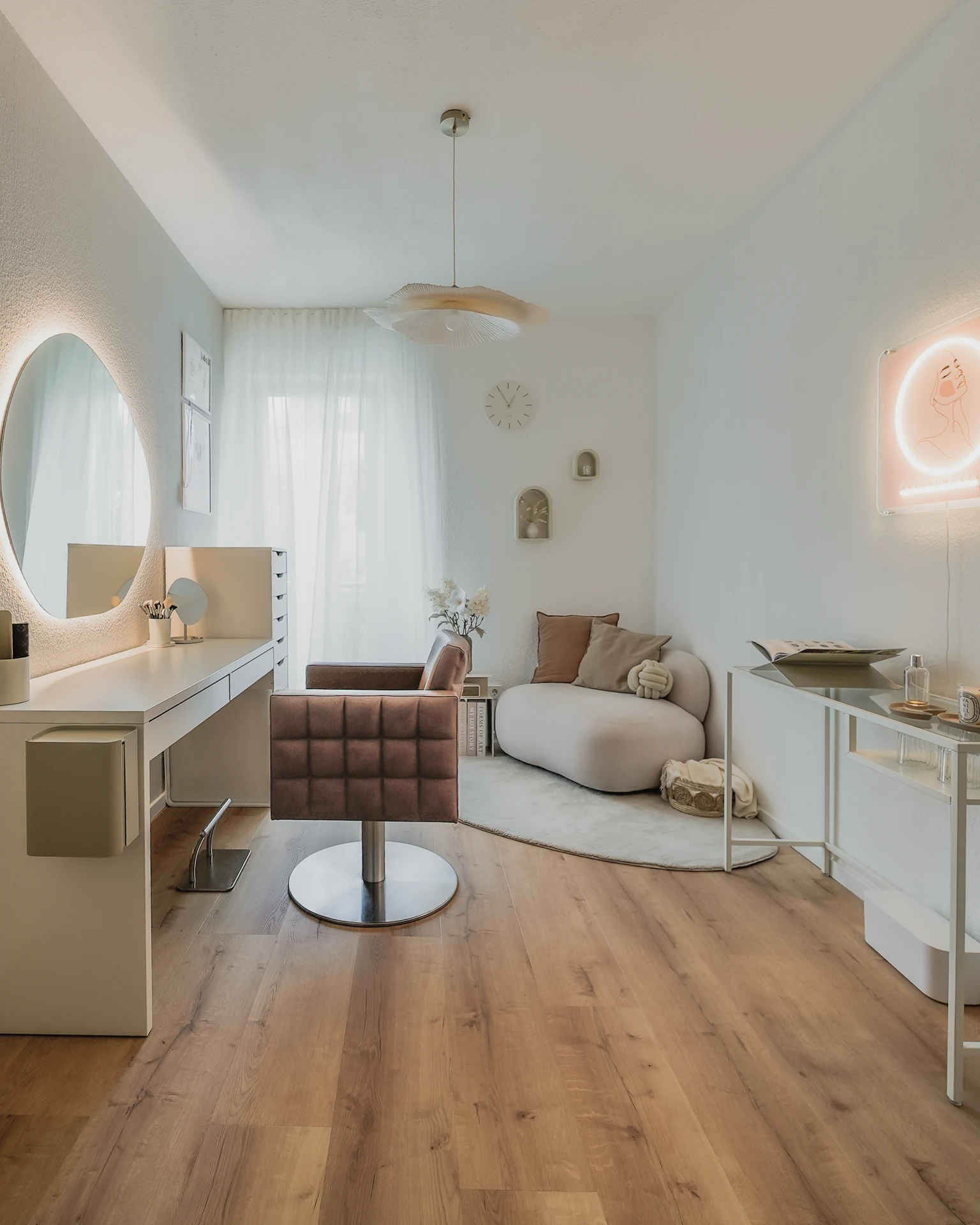 Heller Stylingraum mit Schminkplatz, Sessel und beleuchtetem Wandlogo.